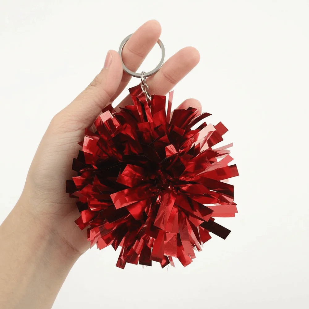 Eine Hand hält einen roten metallischen Pom-Pom-Anhänger mit einem silbernen Ring.