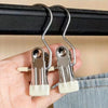 A hand holds a set of stainless steel clothespins with white grips, hanging from a black bar.