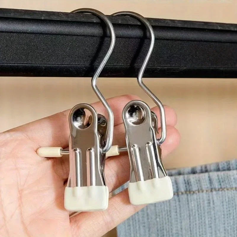 A hand holds a set of stainless steel clothespins with white grips, hanging from a black bar.