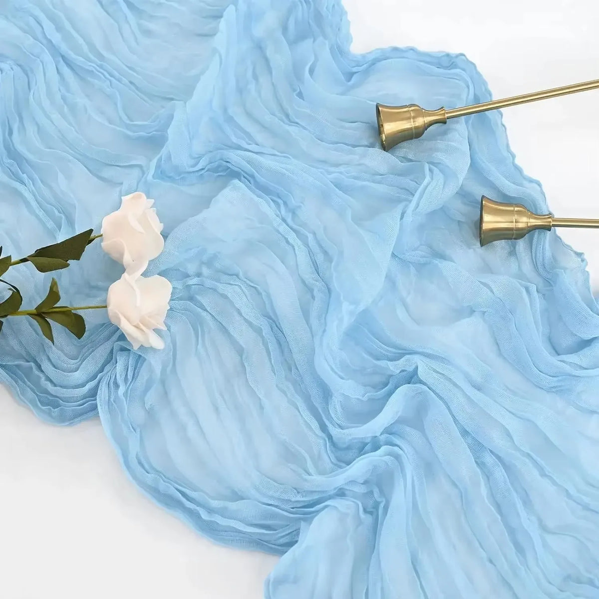 Light blue sheer fabric draped with white roses and gold-toned hardware for a boho table runner set