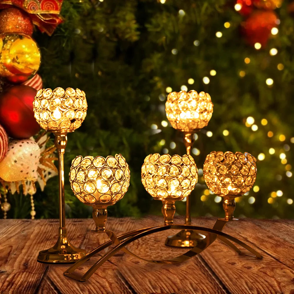 A set of gold crystal tealight candlesticks displayed on a wooden surface in front of a festive green Christmas tree.
