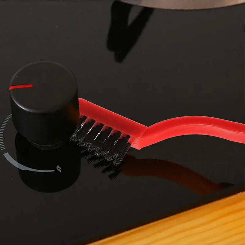 Un cepillo de cocina de silicona rojo con mango negro y cerdas sobre una superficie oscura.