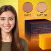 Une femme sourit à côté d'une boîte de détachant Kojic Acid et d'un pain de savon facial jaune.