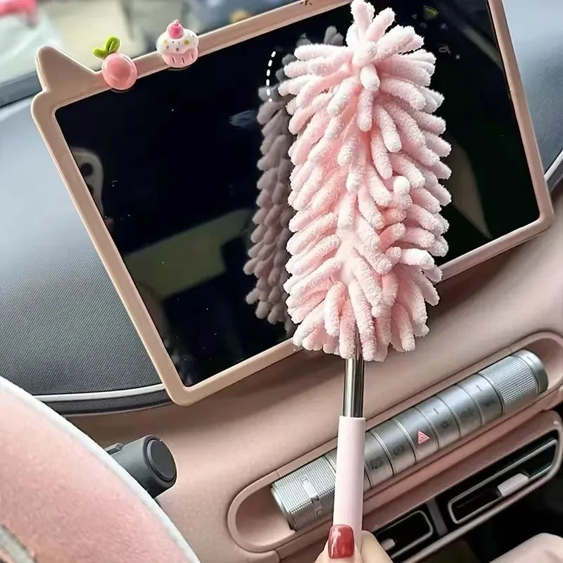 A pink extendable microfiber duster brush is shown resting on a tablet screen in a car interior.