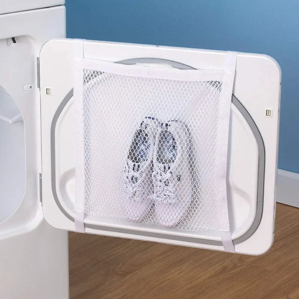A white shoe drying net is placed inside the door of a white dryer appliance.