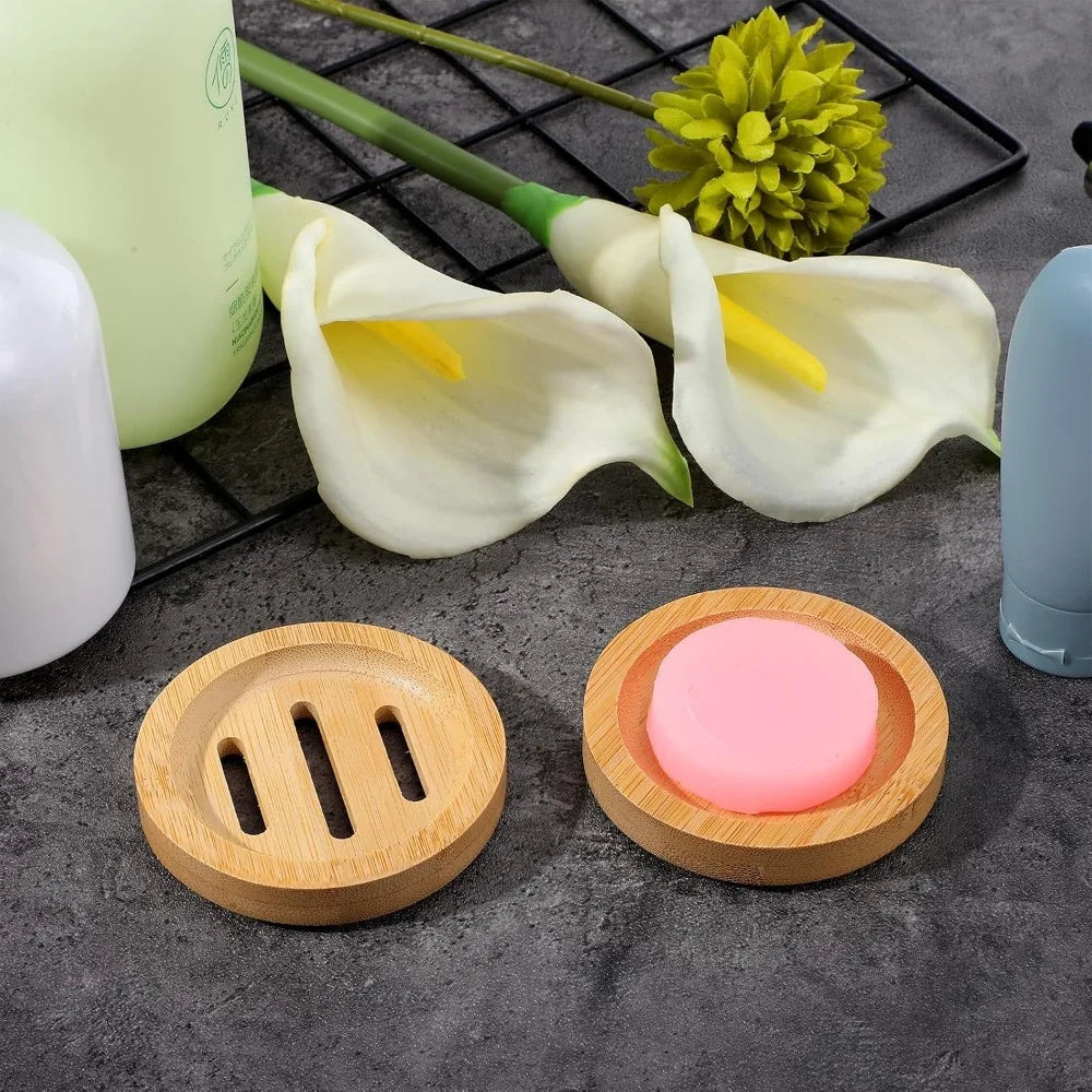 A set of natural wooden soap dishes featuring a pink soap bar and white tulip-shaped flowers on a dark surface.