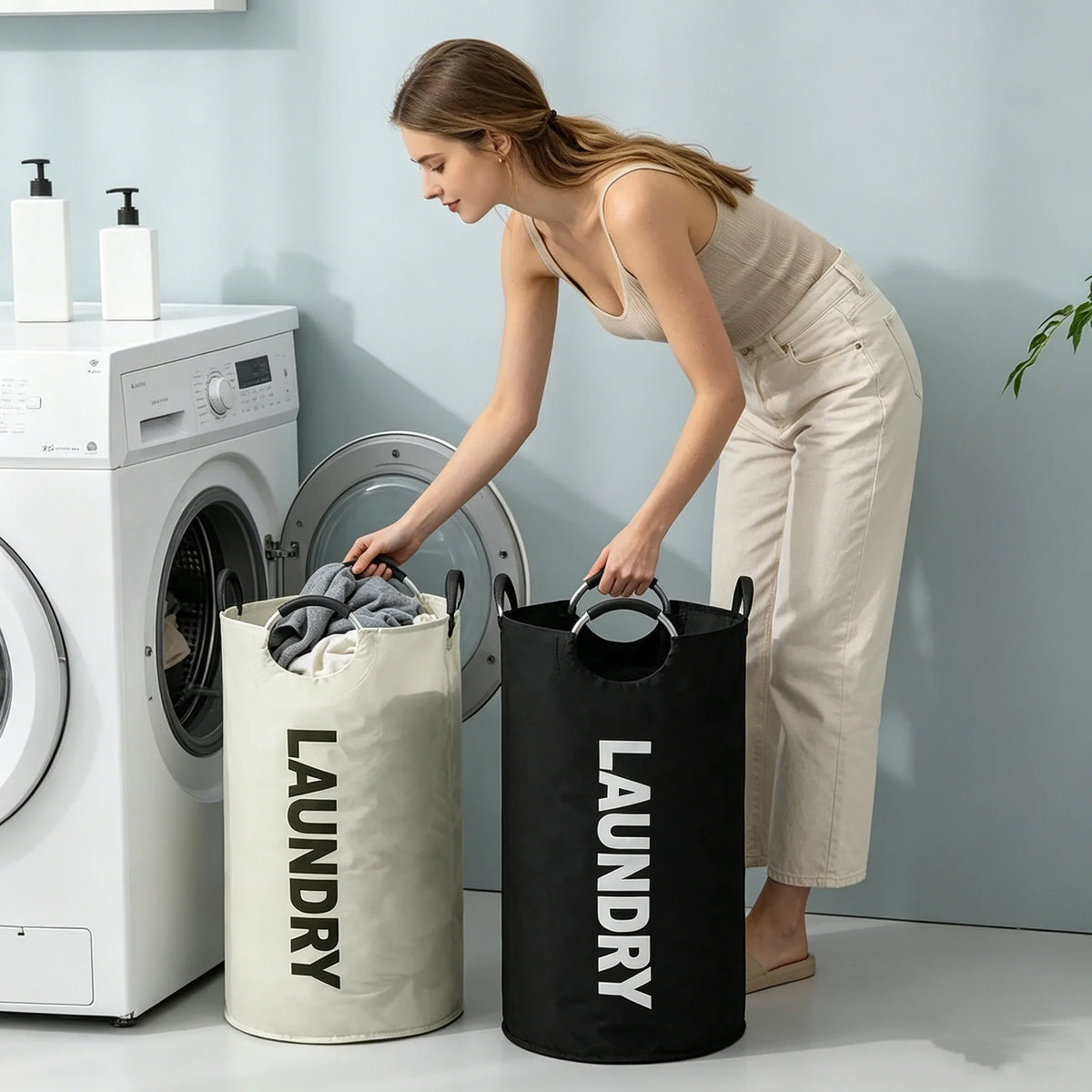 A woman is placing laundry into a large black laundry basket next to a white washing machine.
