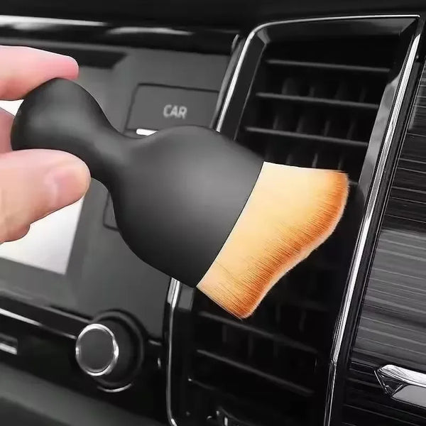 A hand is holding a black multi-surface cleaning brush with a light wood-colored bristles, positioned inside a black dispense