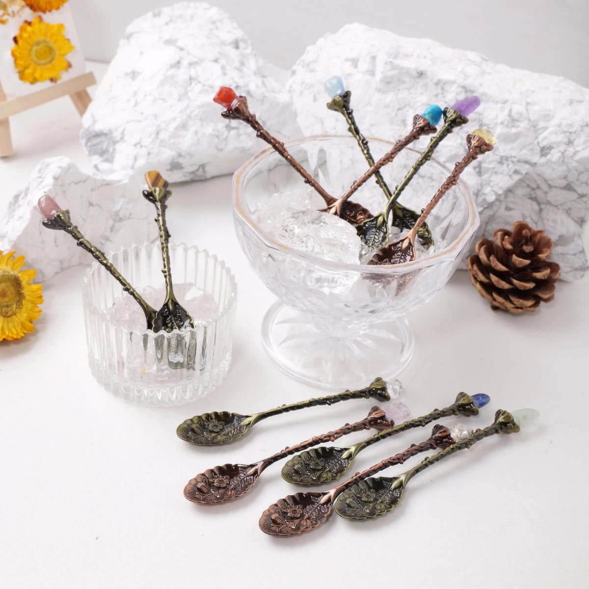 Natural crystal spoons with various colored crystals arranged on white rocks and glass bowls.
