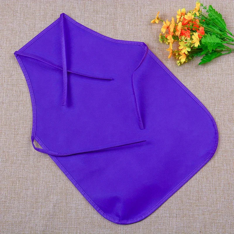 Purple non-woven craft aprons laid flat on a beige fabric with a sprig of yellow flowers.