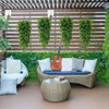 Enredaderas verdes artificiales colgando decorando una pared de jardín con muebles de mimbre y una guitarra