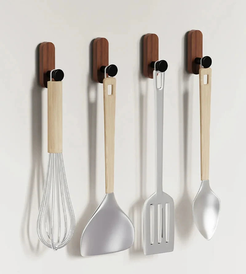 A set of three walnut wood wall hooks with black mounting hardware and stainless steel utensils.