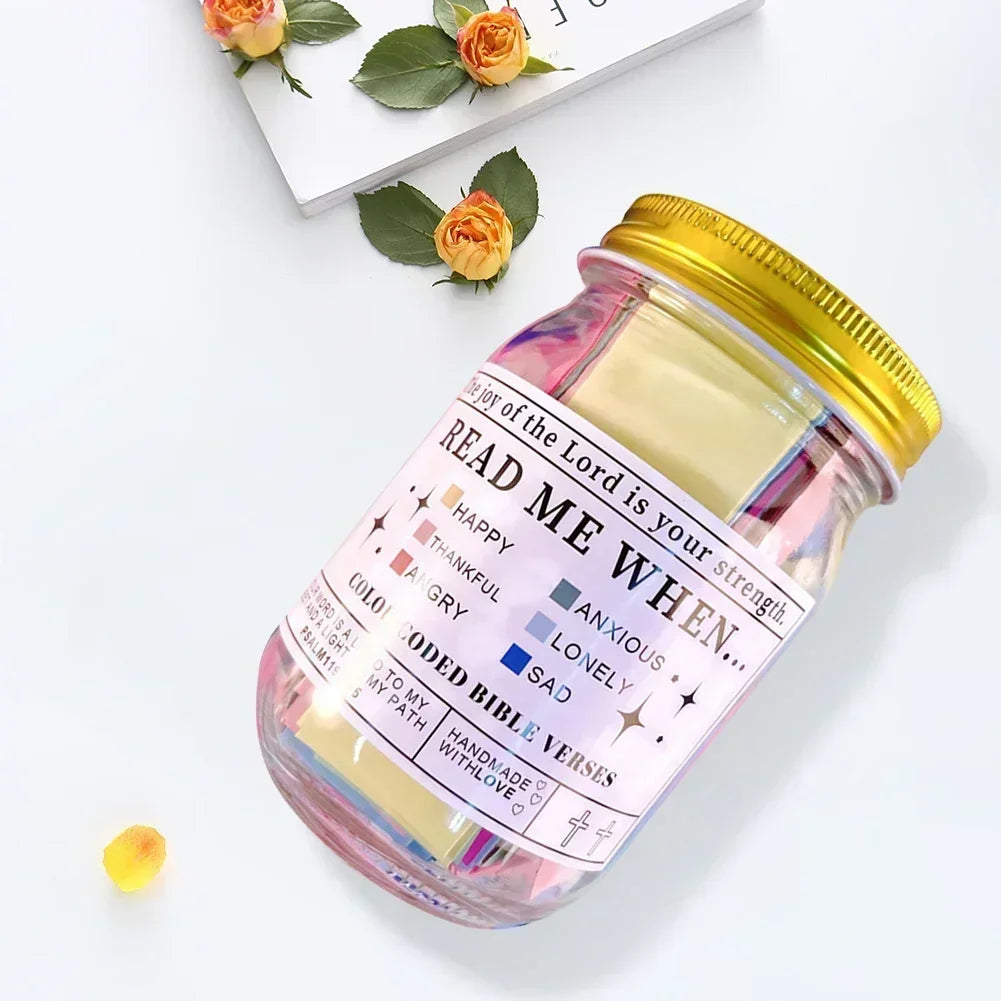 A glass jar filled with colorful scripture verses and a gold lid, resting on a white surface.