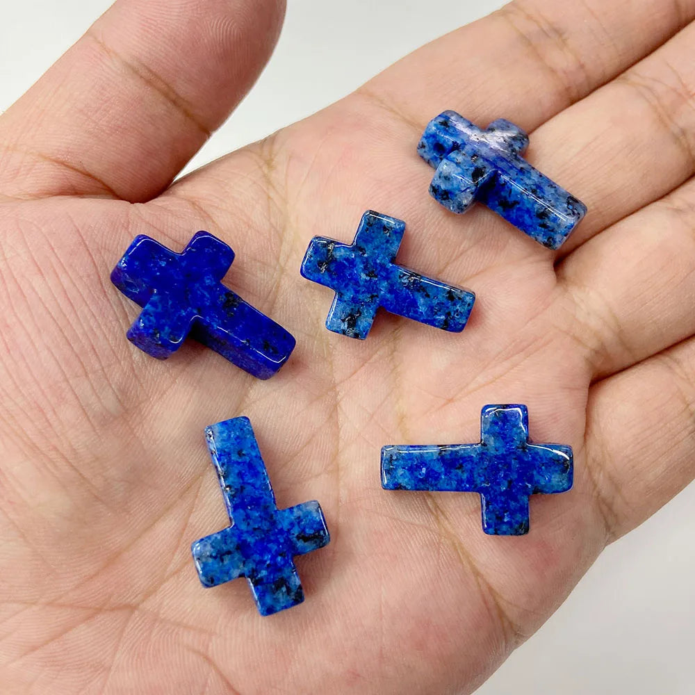 A hand holds several blue and purple natural agate and jasper cross pendant charms.