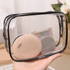 A hand holds a clear plastic travel makeup organizer bag containing a beige powder compact and a silver compact.