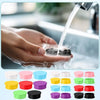 A variety of reusable silicone vial caps in various colors are shown alongside a hand washing them under running water.