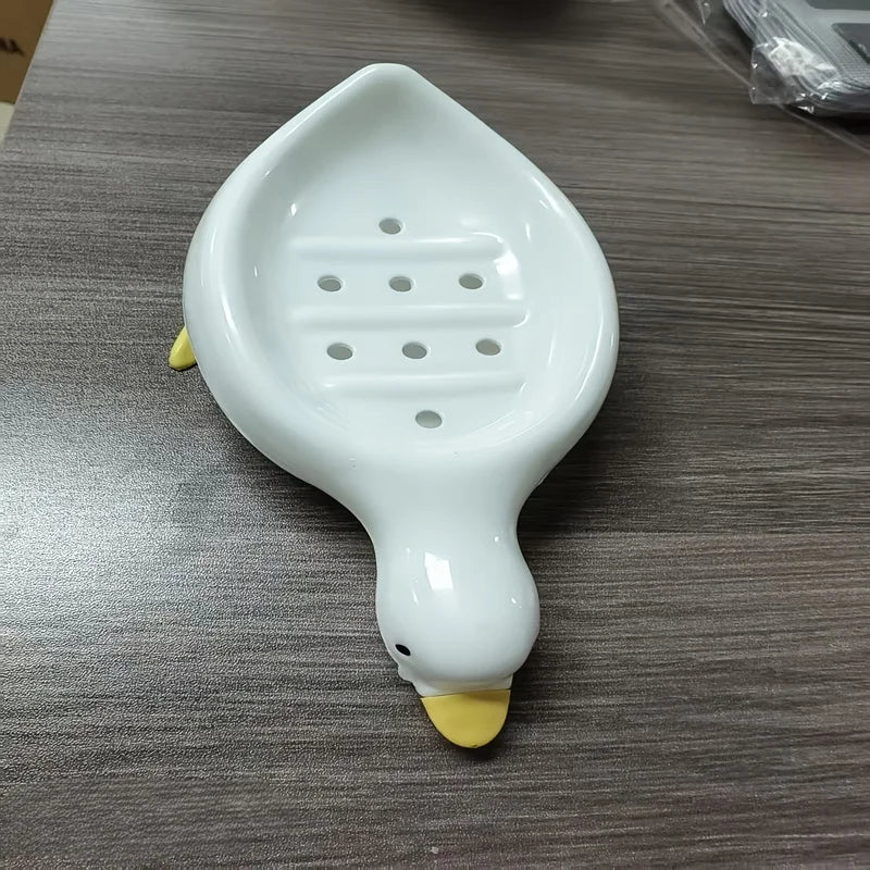 A white duck-shaped soap dish with a self-draining tray is shown on a gray surface.