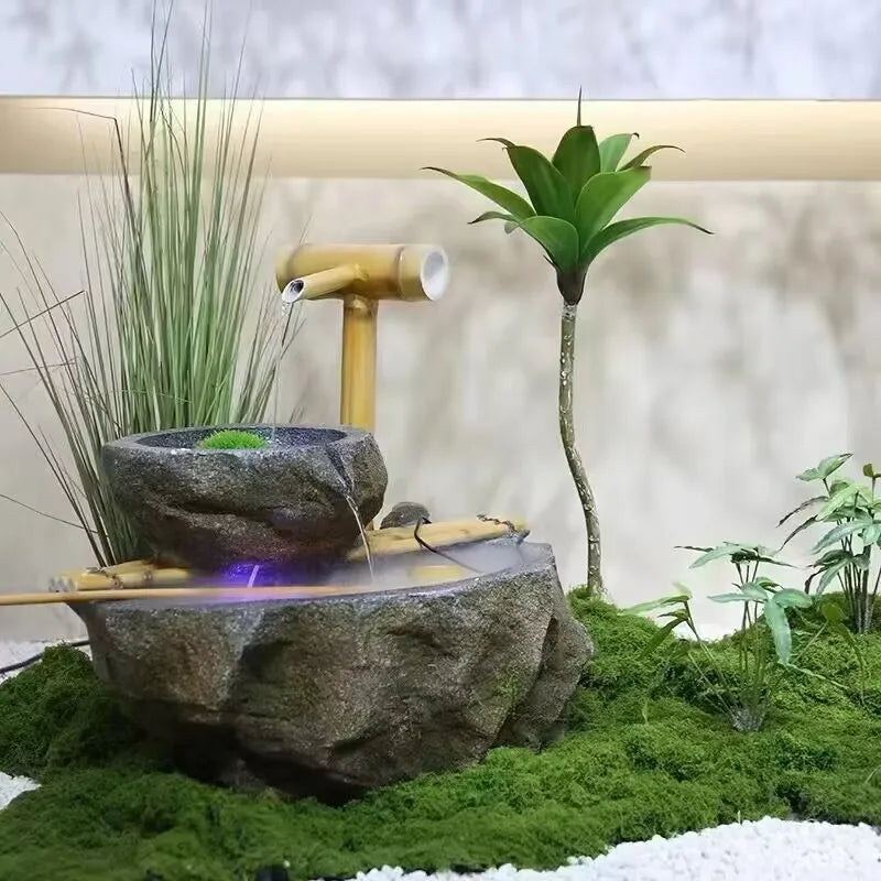A miniature landscape featuring a moss-covered rock, a bamboo pipe, and a leafy plant on a white surface.