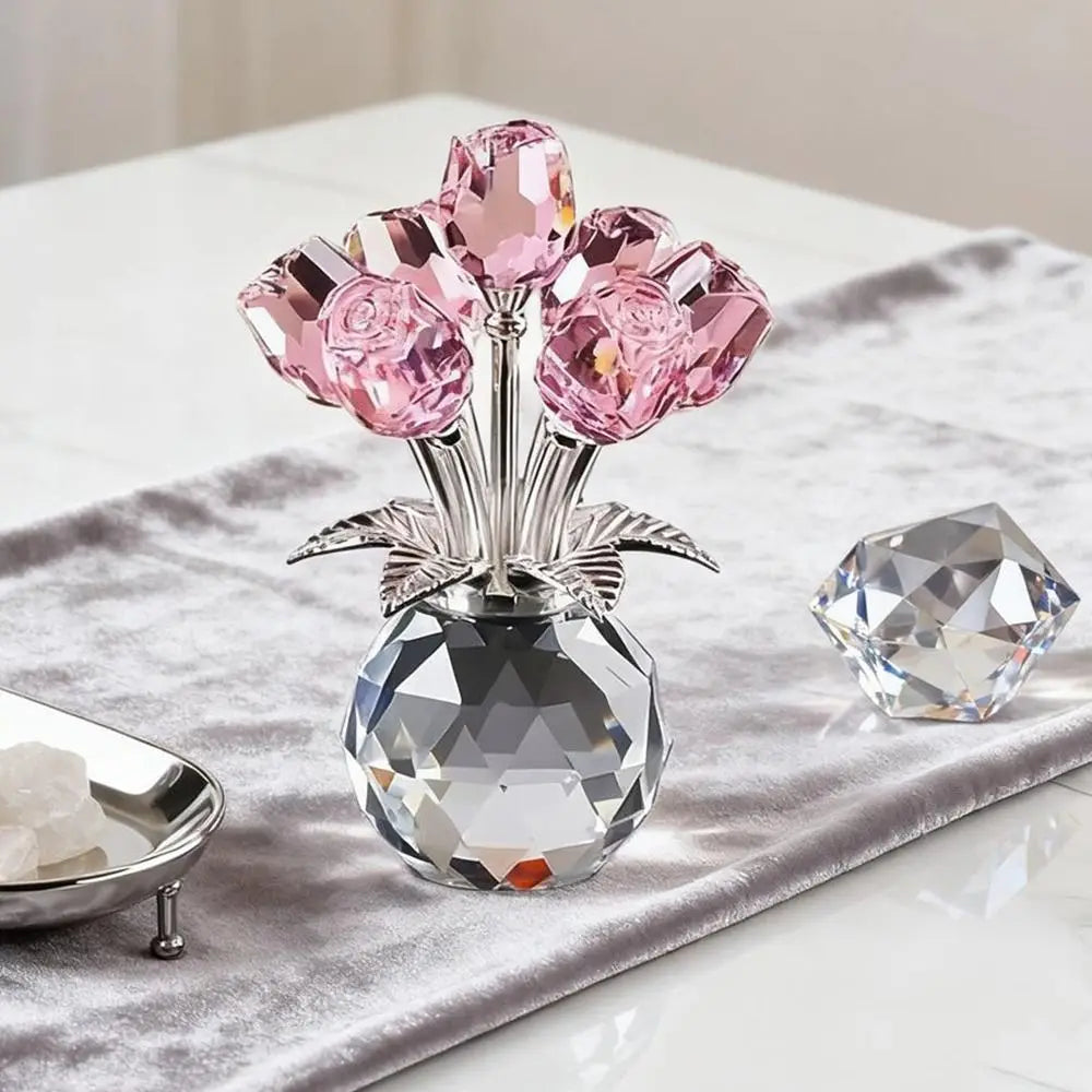 Klares Kristall-Skulptur mit rosa rosenförmigen Kristallen in einer Glasvase auf graufarbener Stoffoberfläche.