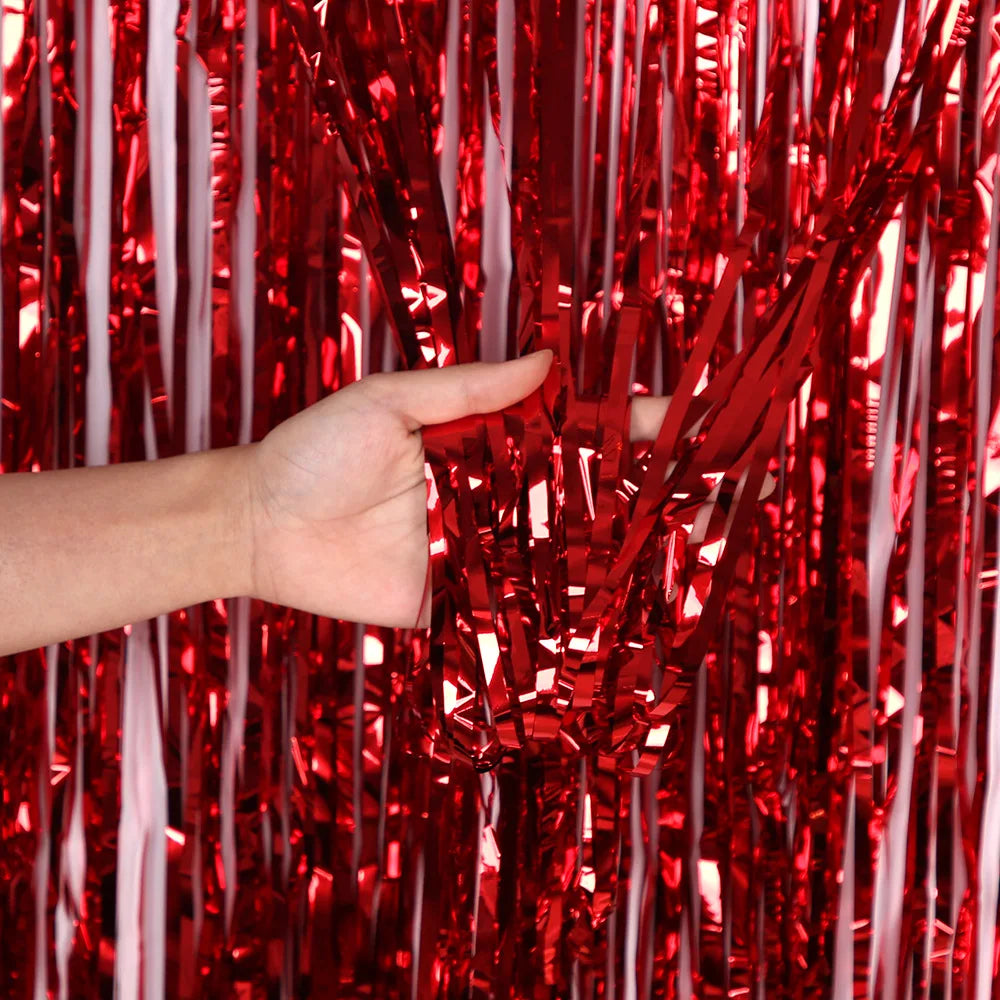 Eine Hand greift durch einen Vorhang aus glänzendem rotem und silbernem Metall-Tinsel-Flimmern.