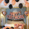 A celebration setup featuring rose gold and black foil balloons spelling out Happy Birthday, with a large number 7 on the bed