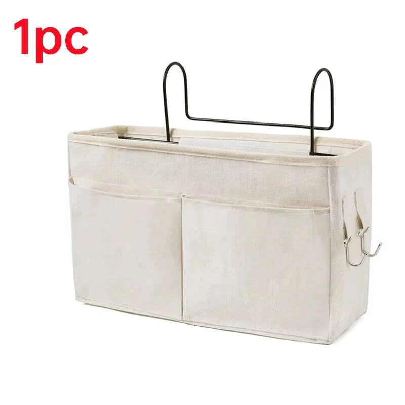 A beige fabric storage basket with a black hanging rack for bedside use.