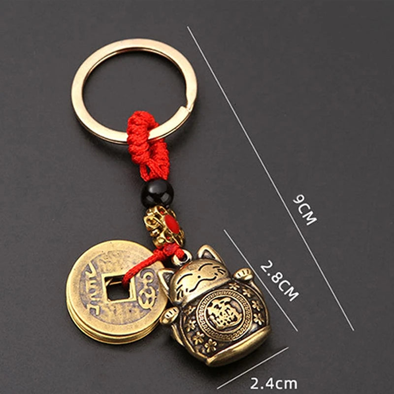 Vintage gold-tone lucky cat keychain featuring a circular tag and a cat charm on a red cord.
