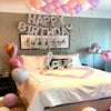 A bedroom decorated for a birthday with foil balloons spelling HAPPY BIRTHDAY LIFE and a heart shape.