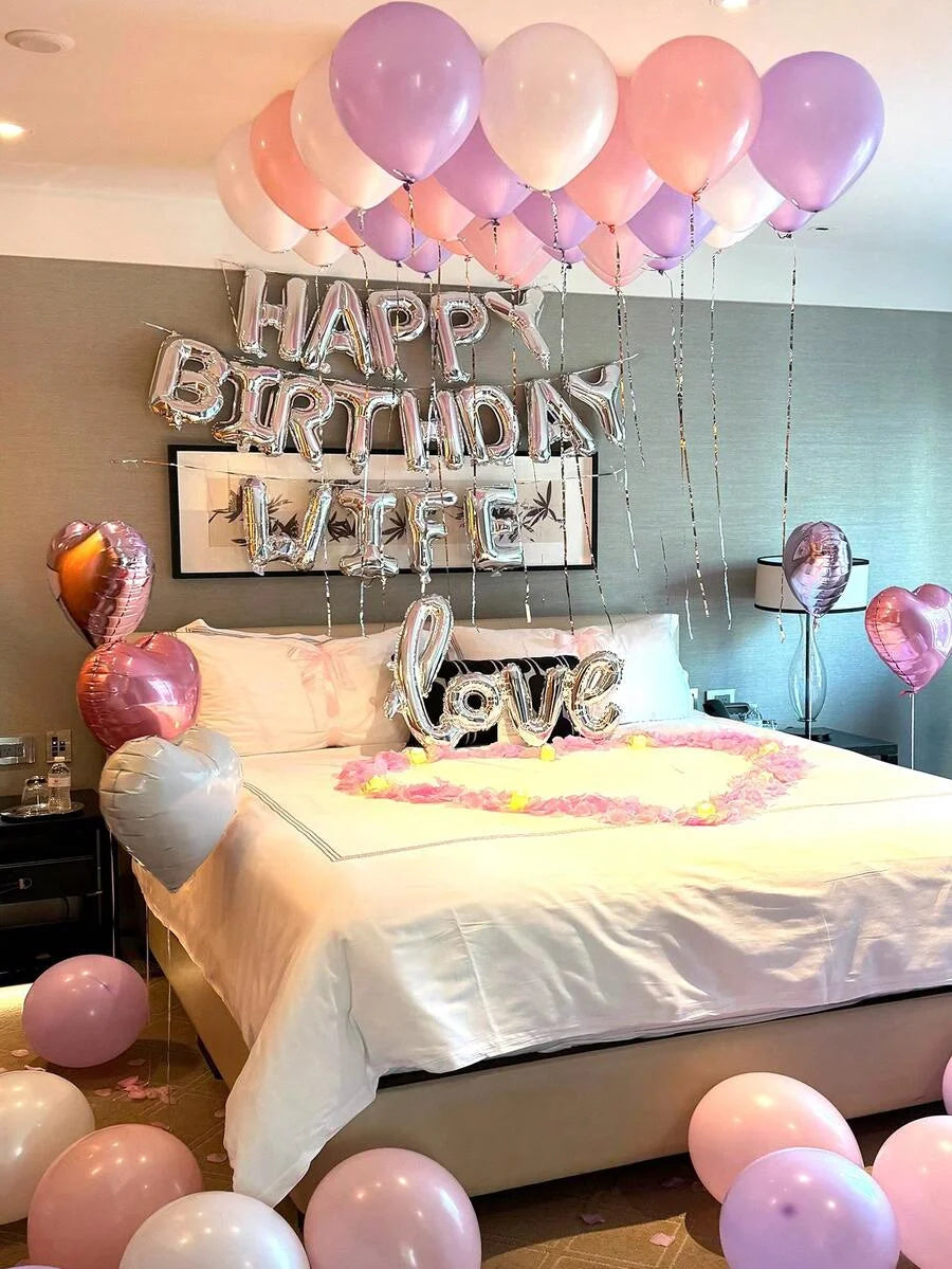 A bedroom decorated for a birthday with foil balloons spelling HAPPY BIRTHDAY LIFE and a heart shape.