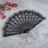 Black lace fabric folding hand fan with red flower accents shown against a gray background.