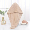 A beige microfiber hair drying wrap towel is displayed on a white surface next to a potted plant and a smooth stone.