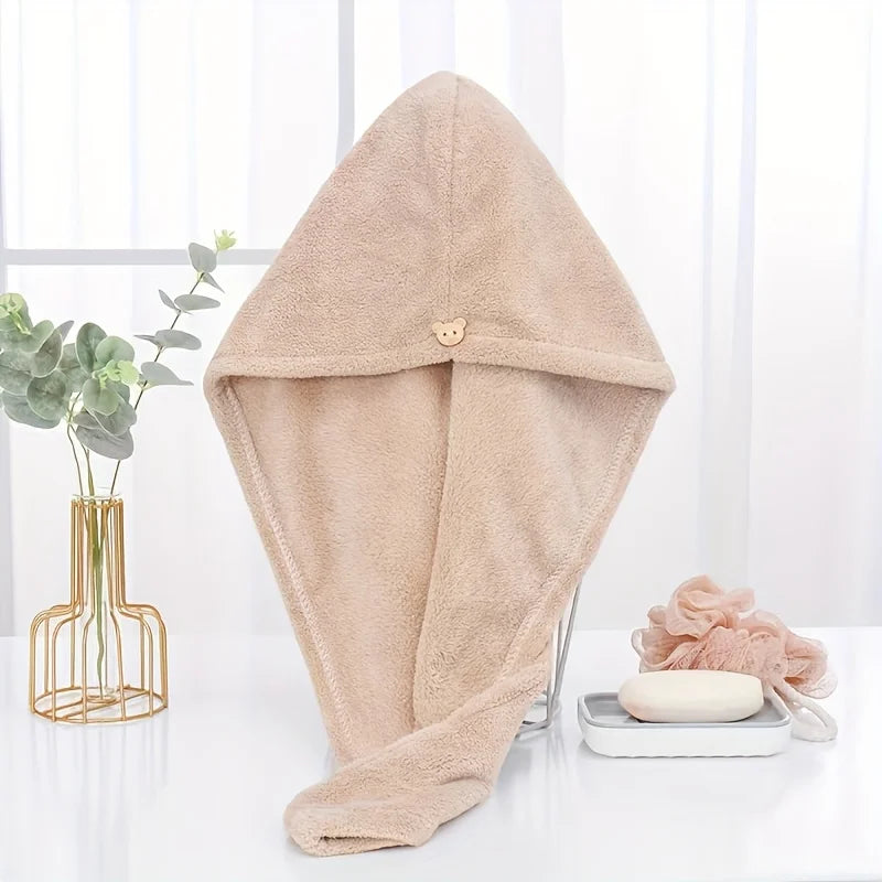 A beige microfiber hair drying wrap towel is displayed on a white surface next to a potted plant and a smooth stone.