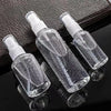 Three clear glass refillable portable spray bottles with white pump tops resting on a dark surface.