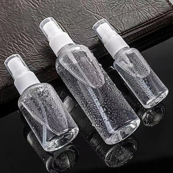 Three clear glass refillable portable spray bottles with white pump tops resting on a dark surface.