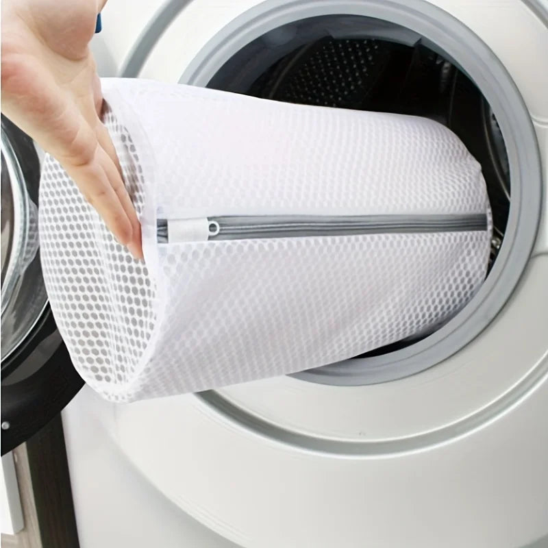 A hand is placing a white mesh shoe cleaning bag into the drum of a washing machine.