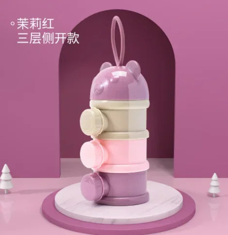 A stack of three purple and pink silicone snack containers for toddlers displayed on a round white marble stand.