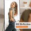 HD reflection of a woman in a green top and jeans standing in a full body wall mirror.