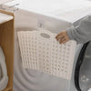 A white folding hand-held clothes storage basket is shown hanging on the door of a washing machine.