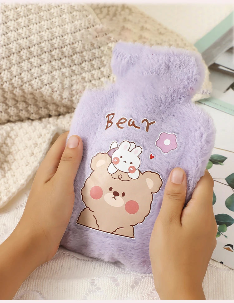 A hand is holding a purple plush cartoon bear hot water bottle with a pink flower design.