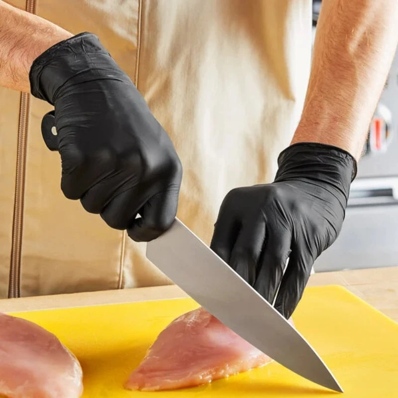 A hand wearing a black nitrile work glove cuts raw meat on a yellow cutting board.