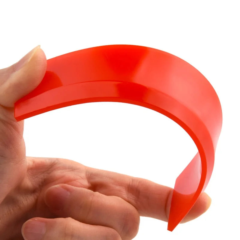 A hand holds a bright red silicone scraper used for grout and gap filling.