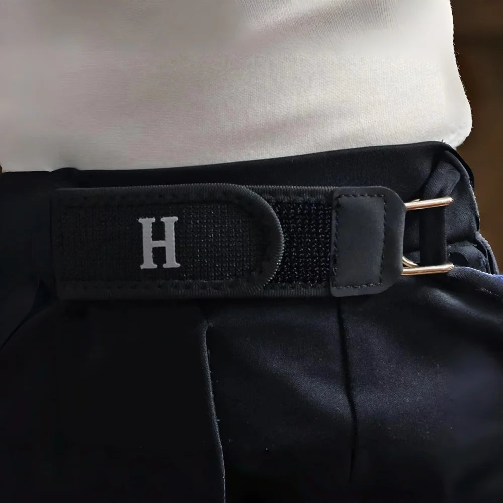A close-up of a black belt with a silver initial H buckle and a black strap on a person's waist.