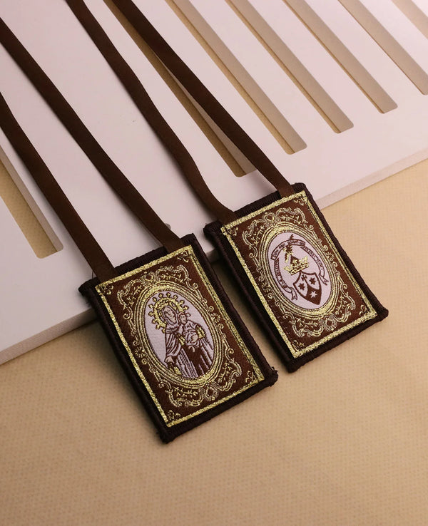 A brown leather scapular necklace with an embroidered religious design is displayed on a light background.