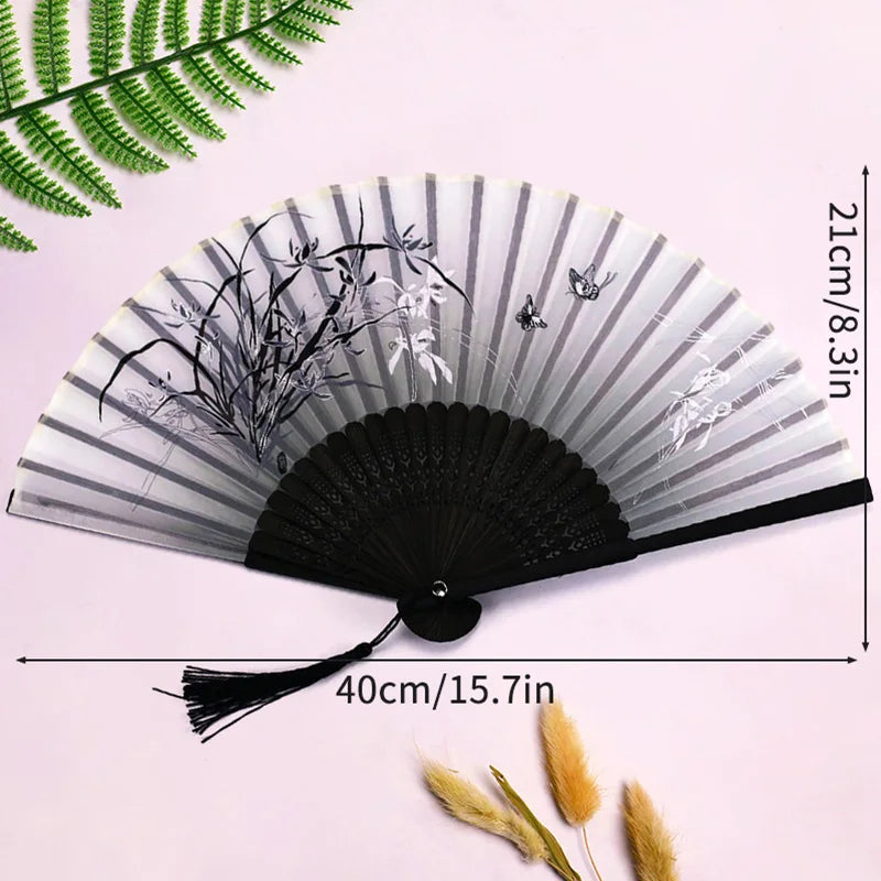 A black and white lace fabric folding hand fan with delicate floral designs shown against a light pink background.