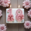 A white candle holder displaying glitter numbers 1 and 8, decorated with pink bows, set against a wooden background.
