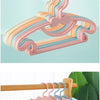 A pink butterfly baby clothes hanger with colorful fabric strips, shown next to a wooden hanger holding a light-colored jacke
