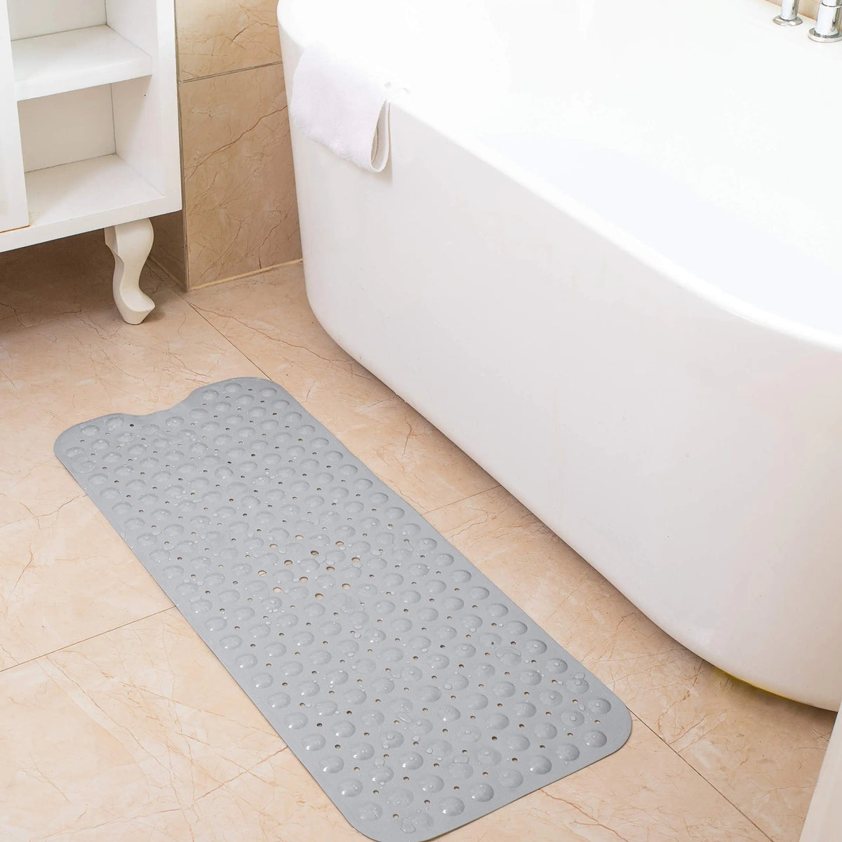 A gray non-slip bathtub mat with suction cups is placed on a tiled floor next to a white bathtub.