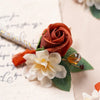 Boutonnière en soie orange vintage avec une rose et une fleur blanche sur feuillage vert.
