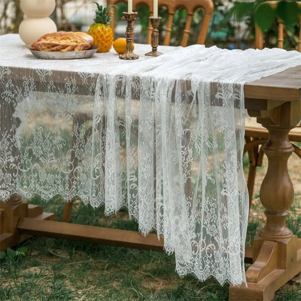 A table covered with a sheer white lace tablecloth set outdoors for a party.