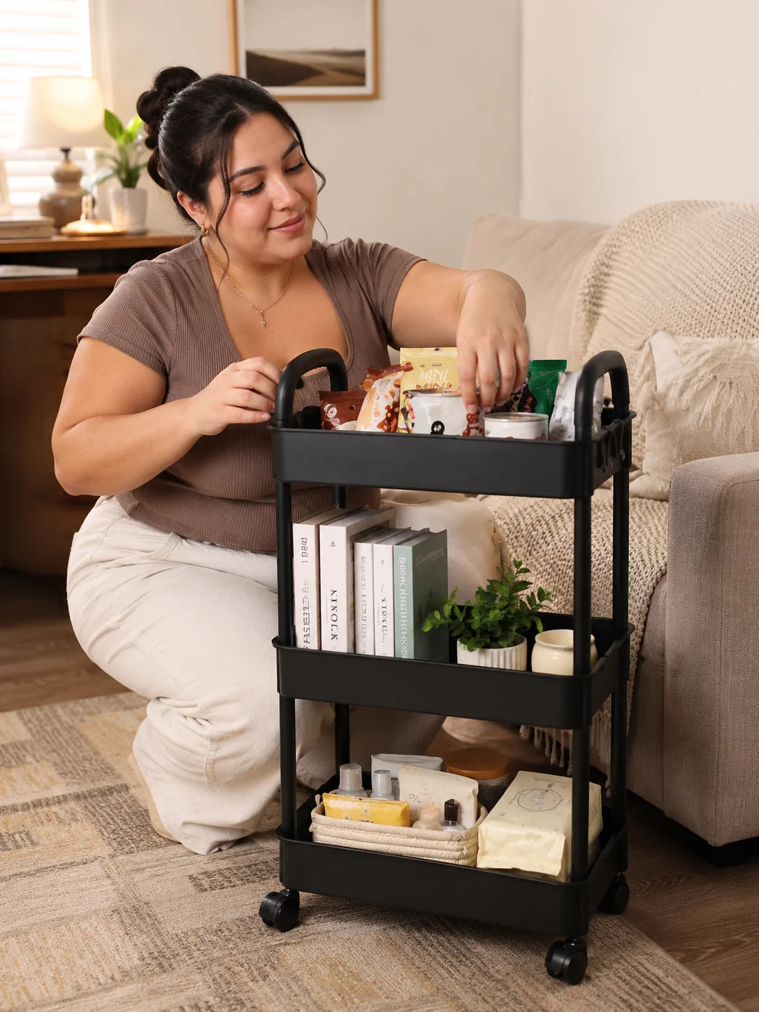 A woman is using a black 3-tier rolling storage cart to organize various items on a wooden floor.